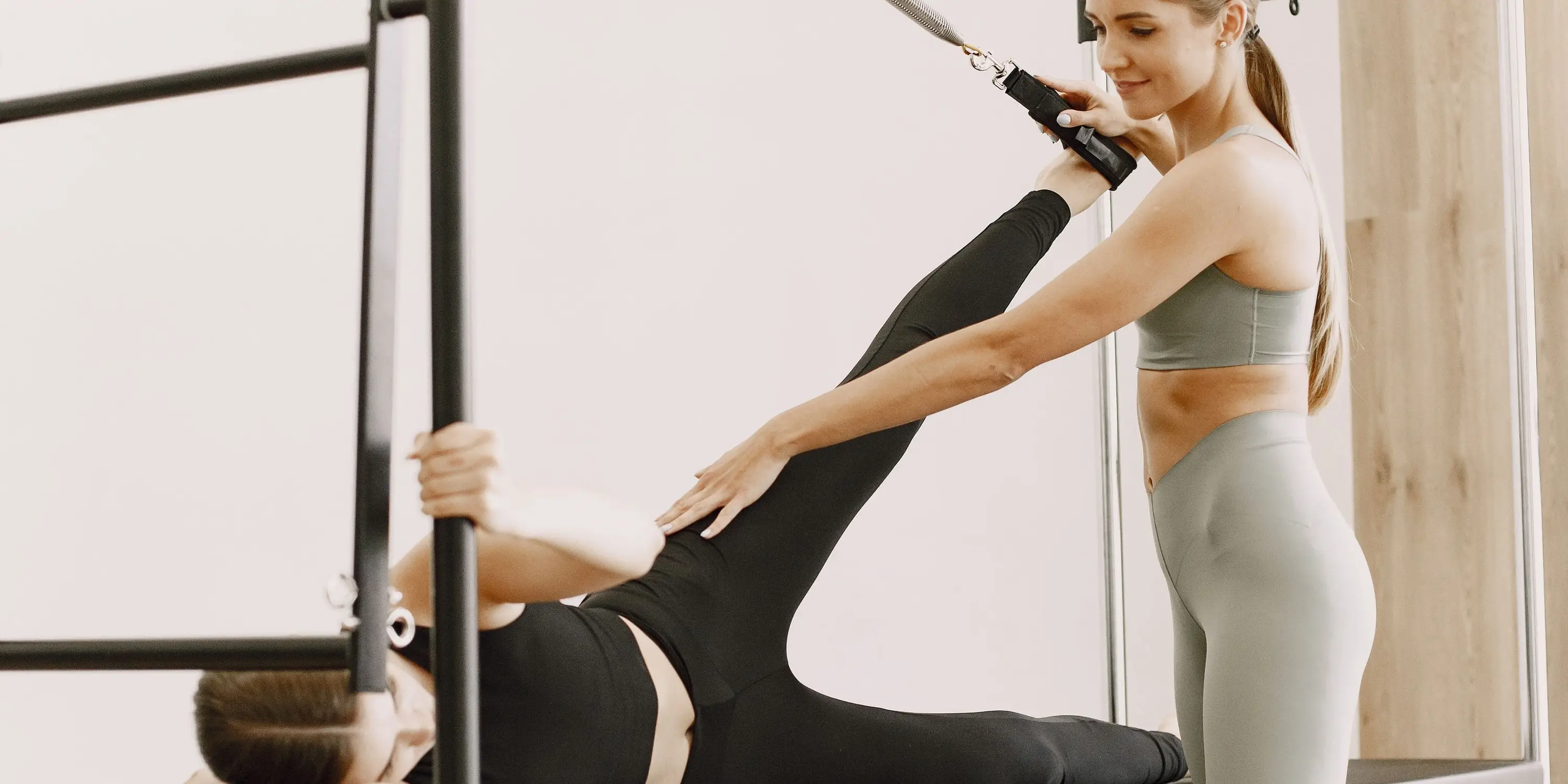An instructor guiding a client's leg through a spring exercise on a tower unit, one to one in a quiet studio.